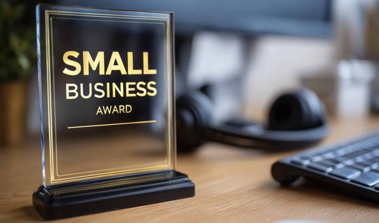 Award plaque on a desk reading SMALL BUSINESS AWARD, with office equipment blurred in the background.