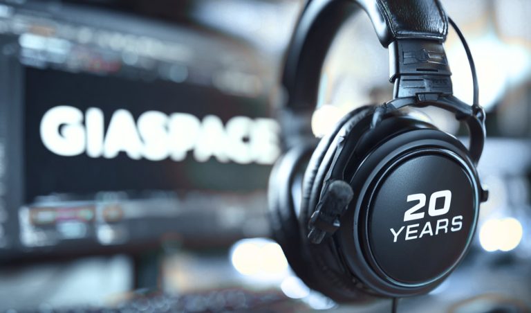 Black over-ear headphones in foreground with bold '20 YEARS' text on the ear cup, blurred computer monitor in the background (celebratory theme).