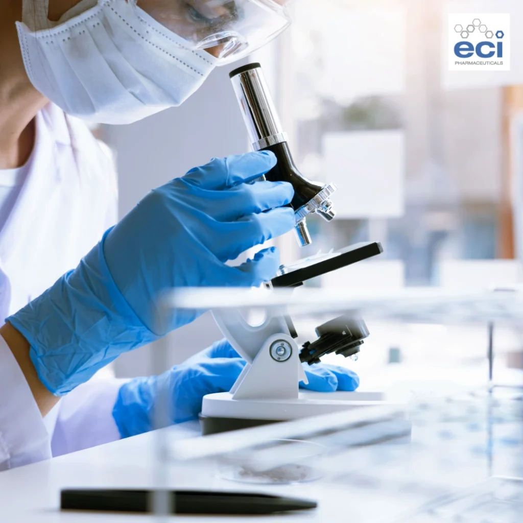 Researcher in a mask and blue gloves examining a slide under a microscope in a laboratory, with the ECI Pharmaceuticals logo visible in the corner.
