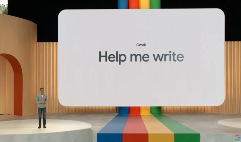 Man standing on a stage beside a large white screen that reads 'Gmail Help me write' with colorful pillars and rainbow floor behind him.