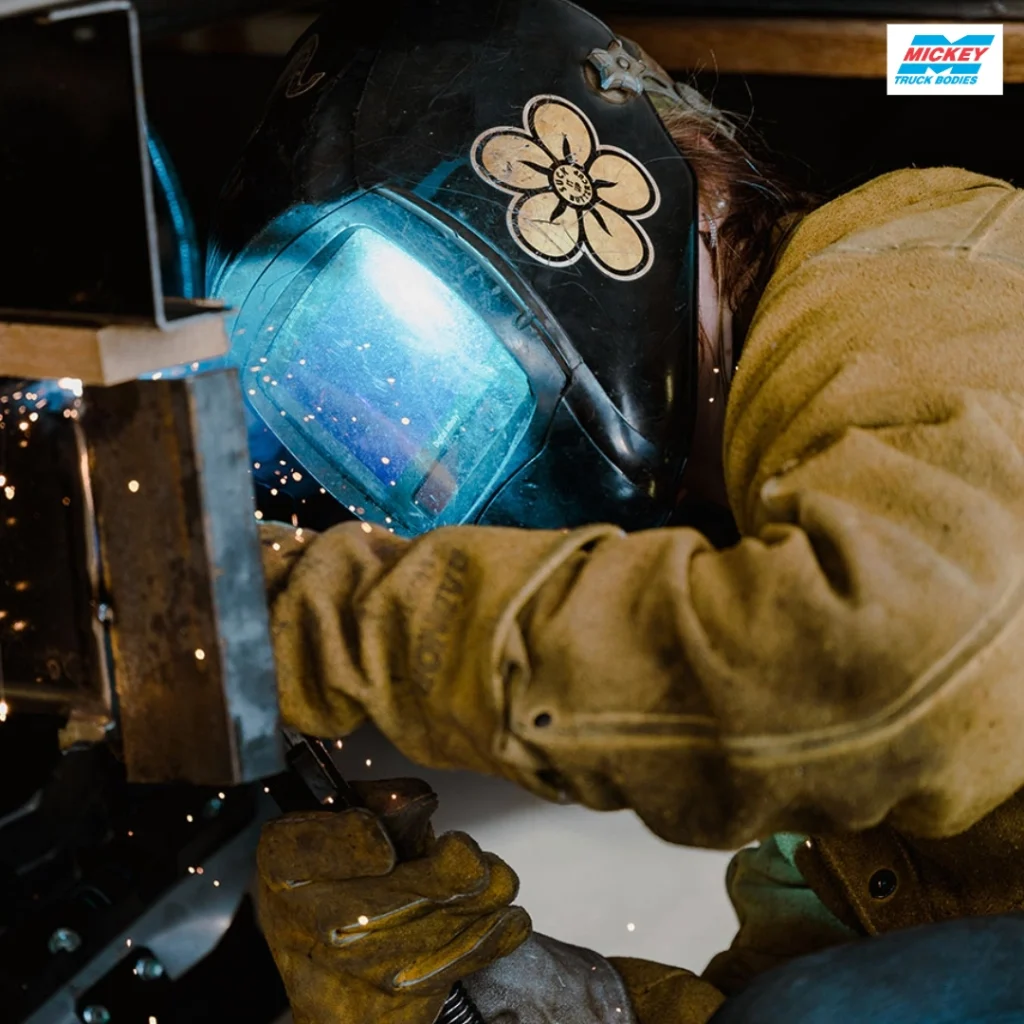 Welder in protective gear welding metal, blue visor glowing with sparks flying around.