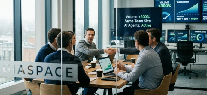 Glass-walled conference room where a diverse team of professionals shakes hands after a meeting around a table, with laptops and charts visible.