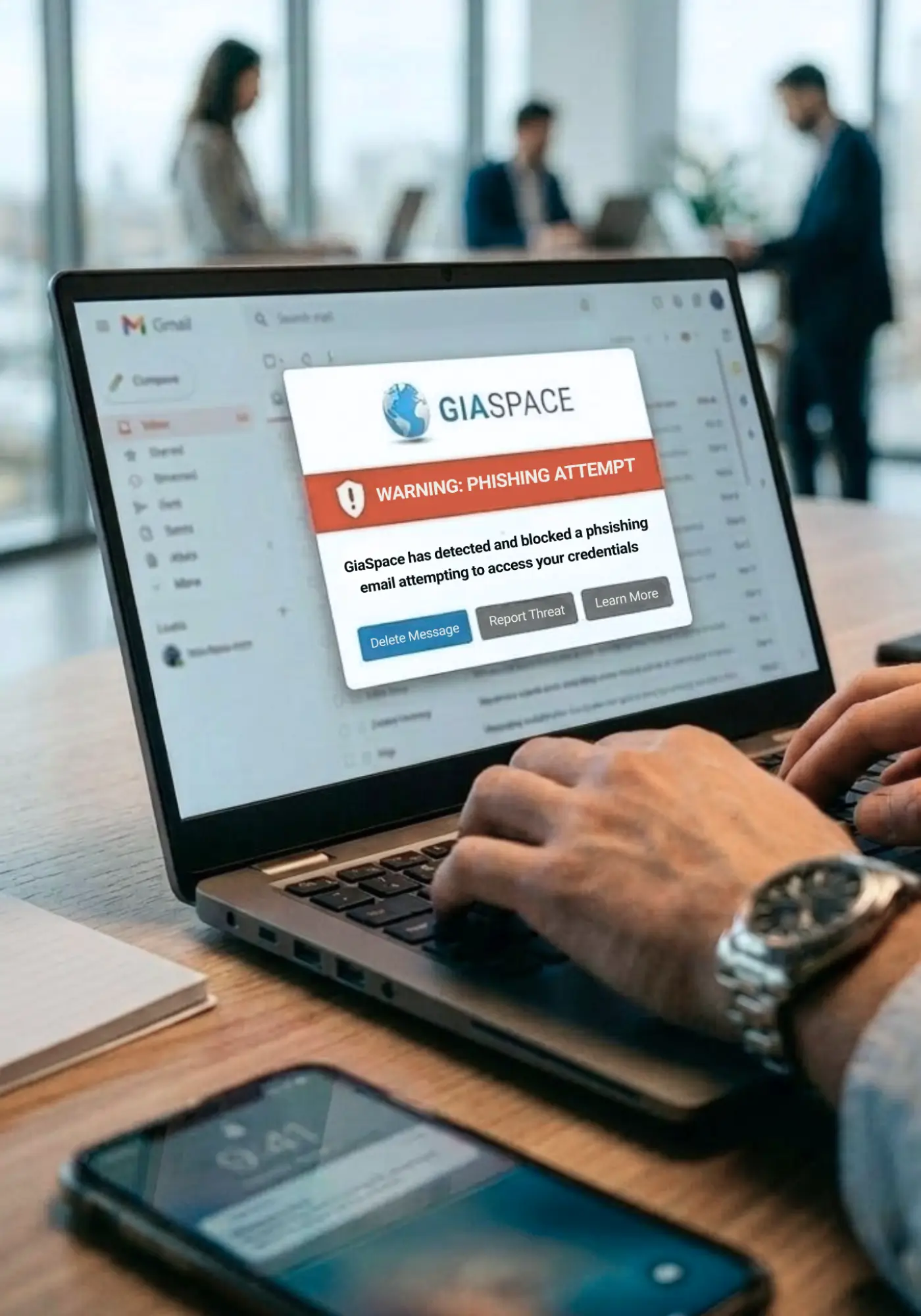 Laptop screen shows a GiaSpace phishing warning popup about an email attempt to steal credentials in an office setting